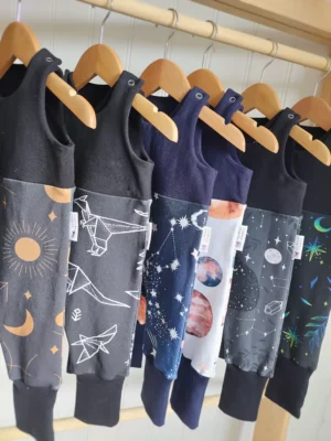 Ensemble de salopettes évolutives en 3/12 mois pour bébé, accrochées sur des cintres. Modèles en coton bio avec des motifs originaux et des couleurs assorties.