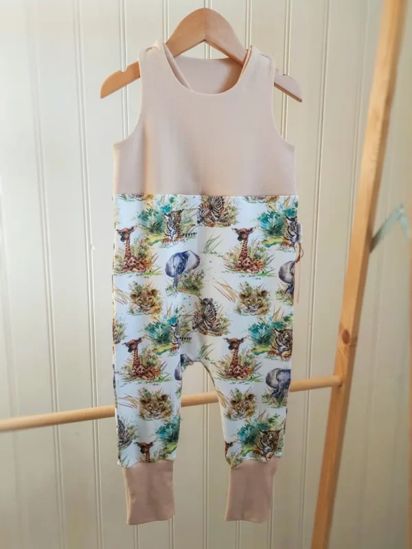 Vue complète de la salopette évolutive 24/36 mois, motif bébé de la savane, couleur beige, suspendue à un cintre sur un portant en bois.
