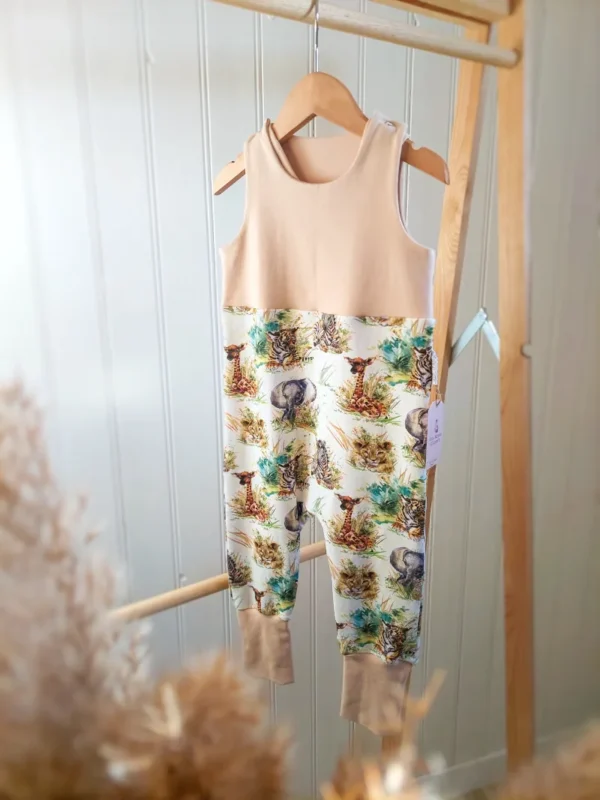 Salopette évolutive 24/36 mois, motif bébé de la savane et couleur unie beige. Accrochée à un cintre sur un portant en bois.